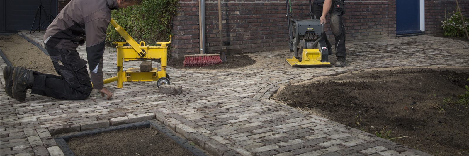 Twee hoveniers leggen nieuwe klinkerbestrating aan voor een woning