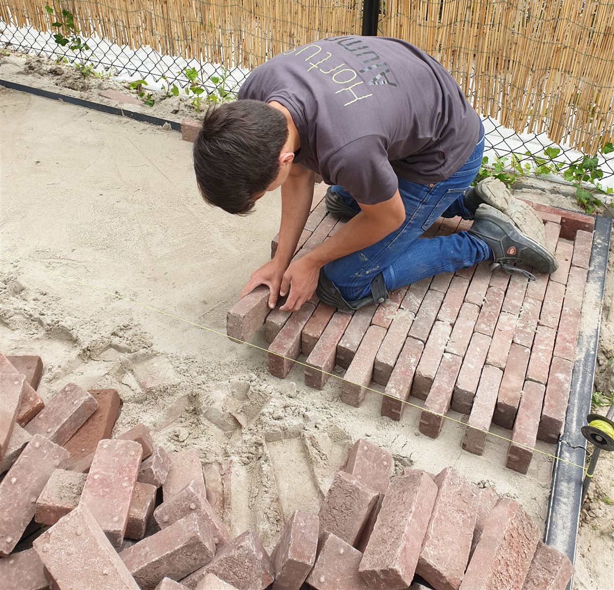Een hovenier legt gebakken klinkers in een tuinpad